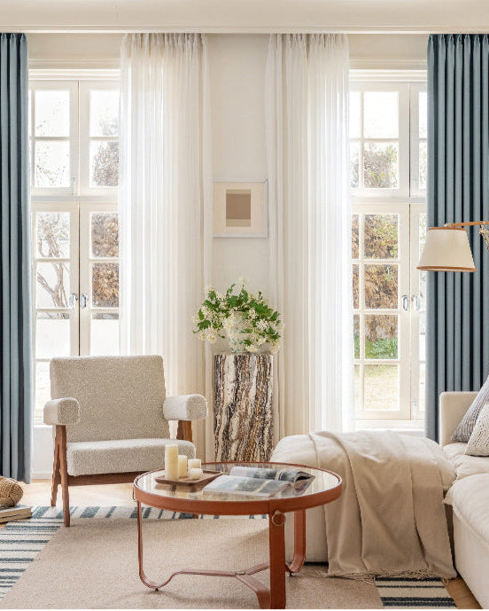 Lightless– Helles Wohnzimmer mit blauen Vorhängen, beiger Couch und natürlichem Licht – schafft eine ruhige und stilvolle Atmosphäre.